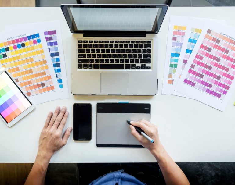 Top view of a young graphic designer working on a desktop computer and using some color swatches, top view.